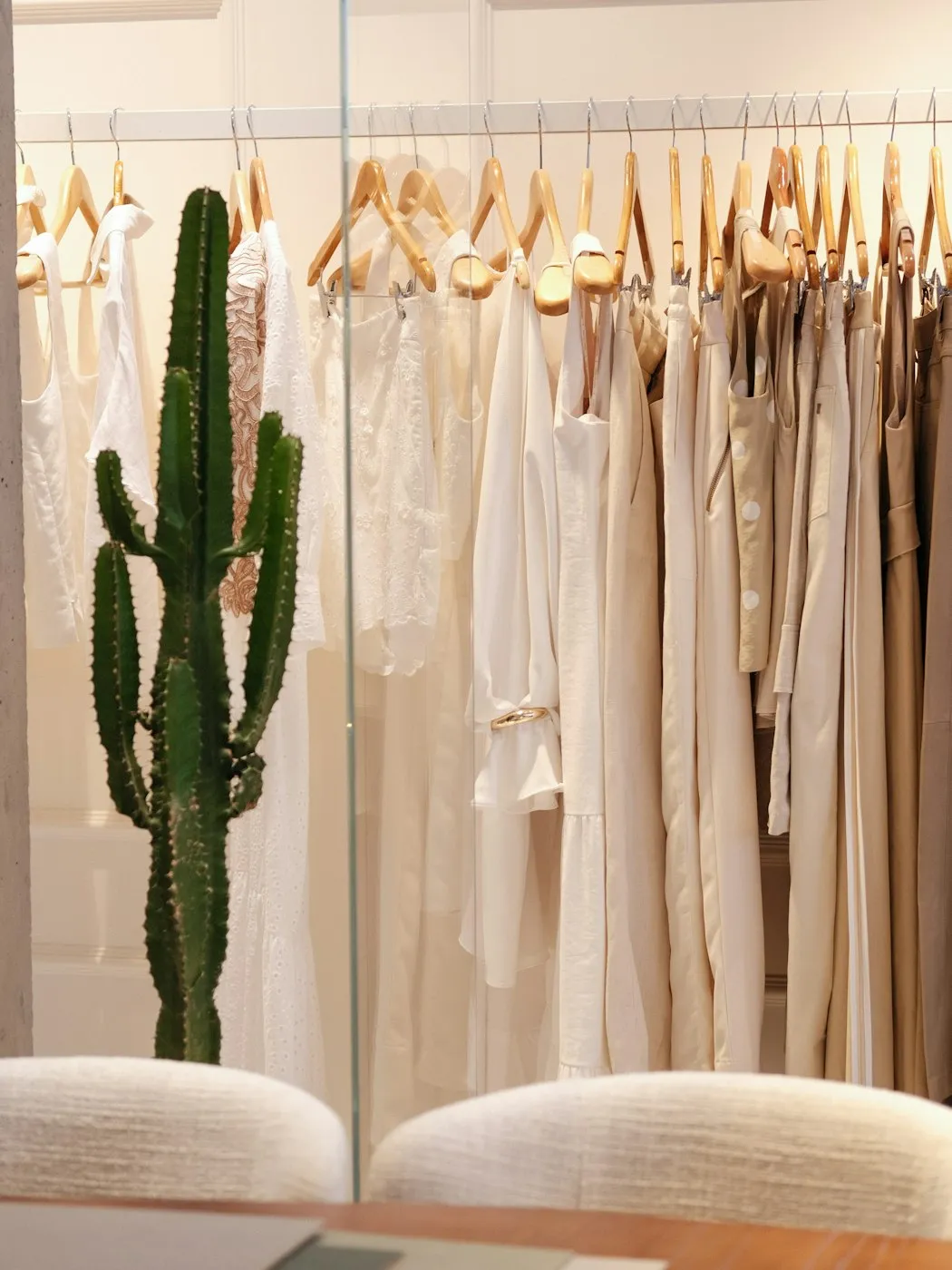 A rail of neutral, considered garments on wooden hangers in a light room.