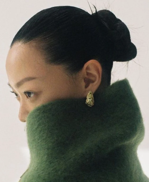 A close portrait framed by a sculptural evergreen collar.